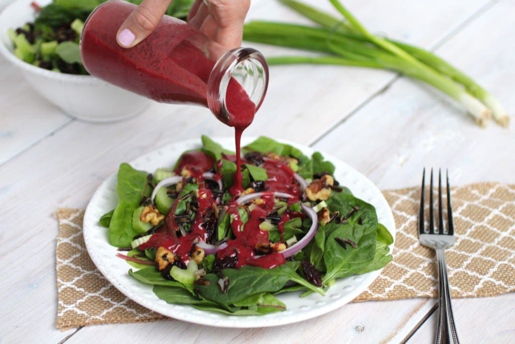 woman pouring a cherry vinaigrette over a spinach and wild rice salad