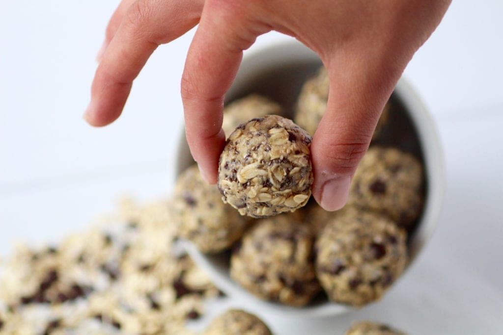 woman holding a no bake tahini energy ball made of tahini, oats, honey, coconut, chia seeds and chocolate