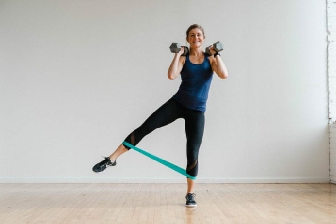 Woman performing a leg lift with dumbbells front racked in a 30 Minute Leg Workout At Home