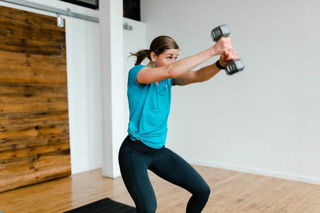Woman performing wood-chop exercise with one dumbbell with text overlay full body HIIT workout for women