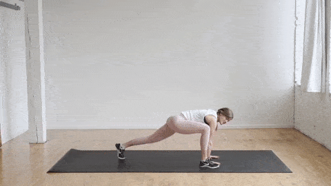 woman performing a plank and lunge jump switch in a warm up routine at home