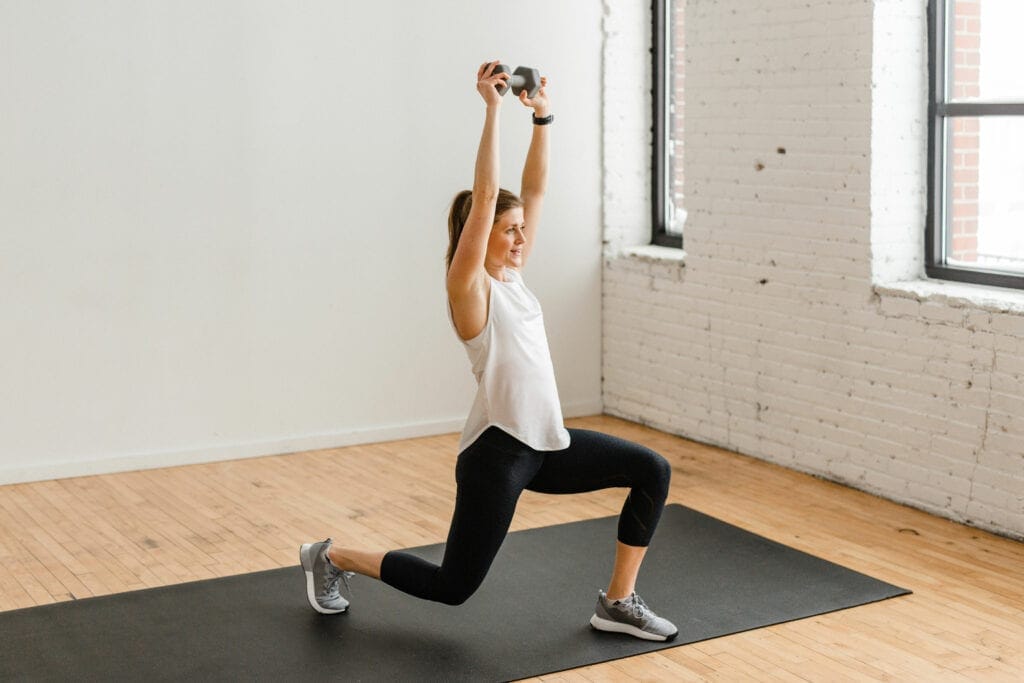 woman performing a lunge exercise and overhead press with a dumbbell in a pyramid workout