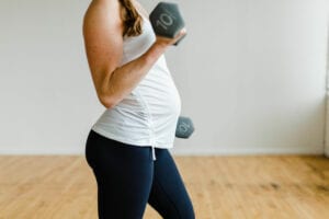 Pregnancy women wearing maternity workout clothes and activewear, doing a single arm bicep curl with 10 pound dumbbells.