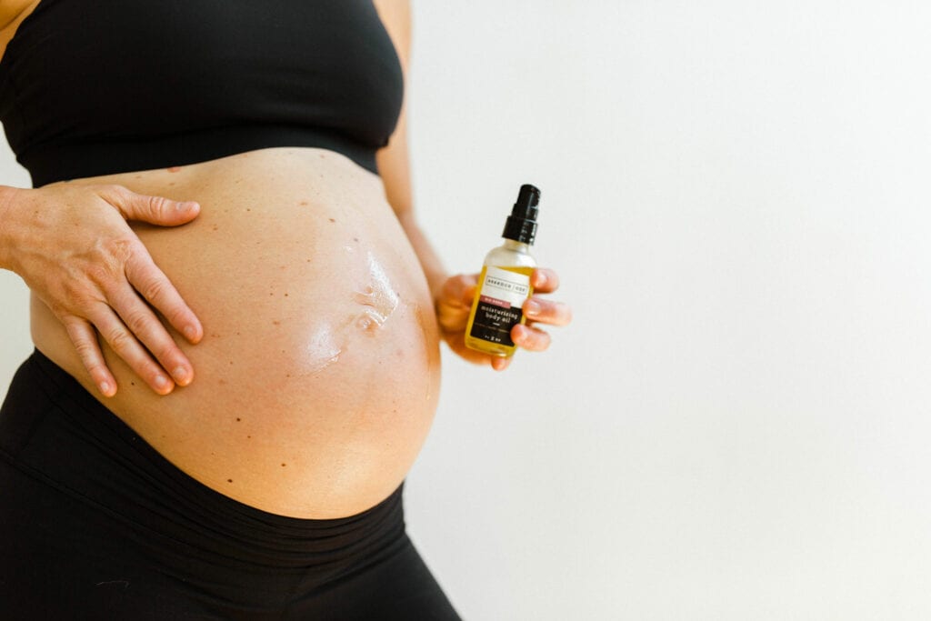 Pregnant women putting natural toning body oil on her belly to maintain a fit pregnancy. 