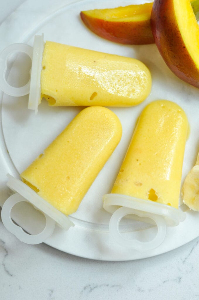 mango smoothie popsicles laying on a plate in popsicle molds