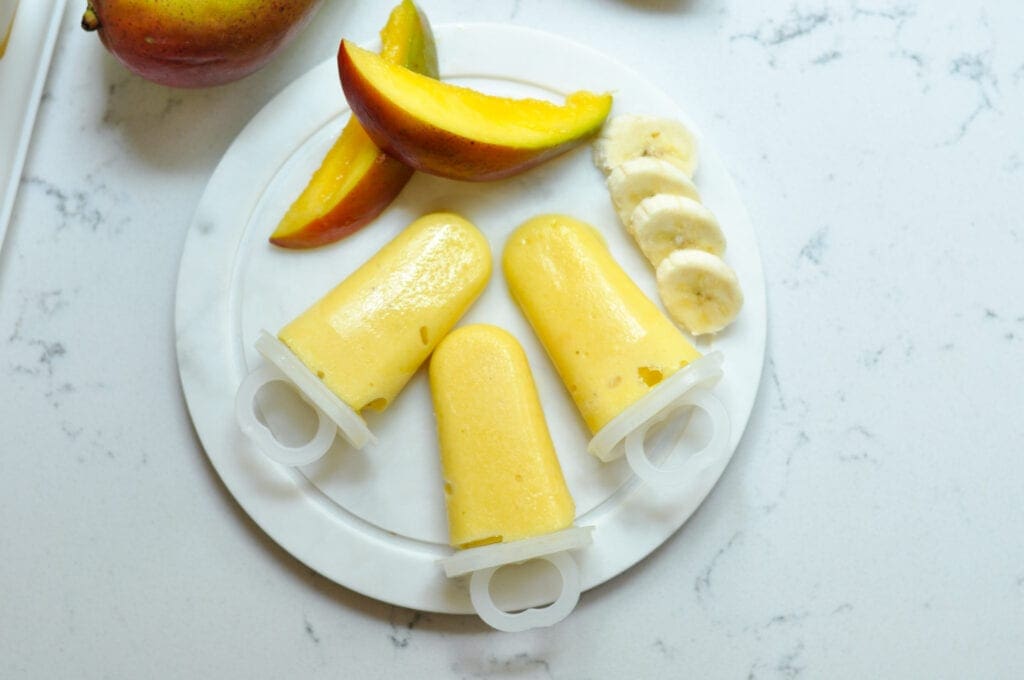 mango smoothie popsicles with mango and banana slices on a plate