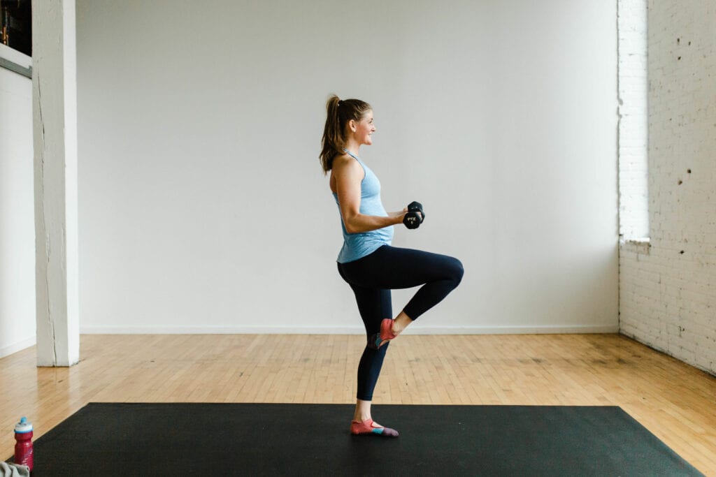 woman performing a knee drive and bicep curl hold in a barre class at home