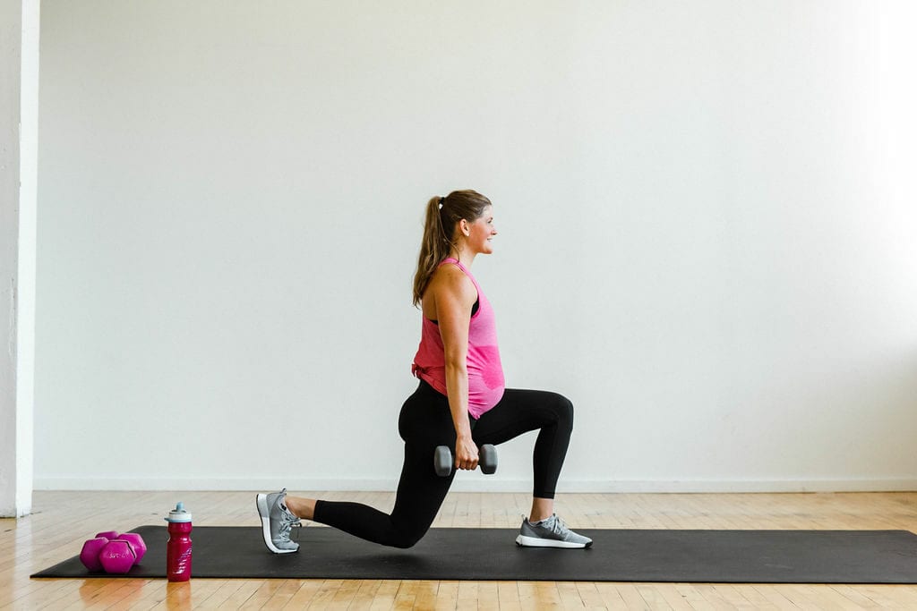 woman performing a lunge with dumbbells | leg day