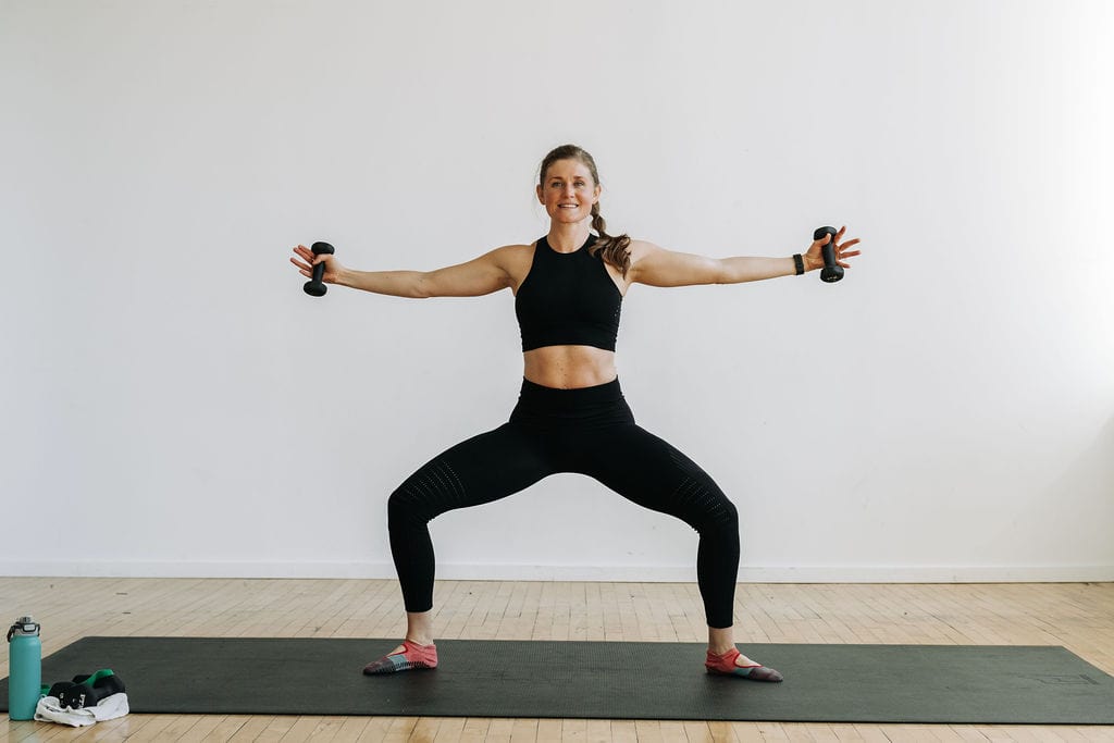 woman performing a second position squat and lateral raise with dumbbells in a barre blend workout