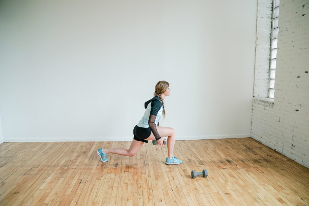woman performing a front lunge and dumbbell pass in a leg workout