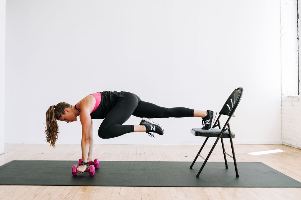woman performing mountain climbers from an incline with her hands on dumbbells in a full body HIIT workout with weights