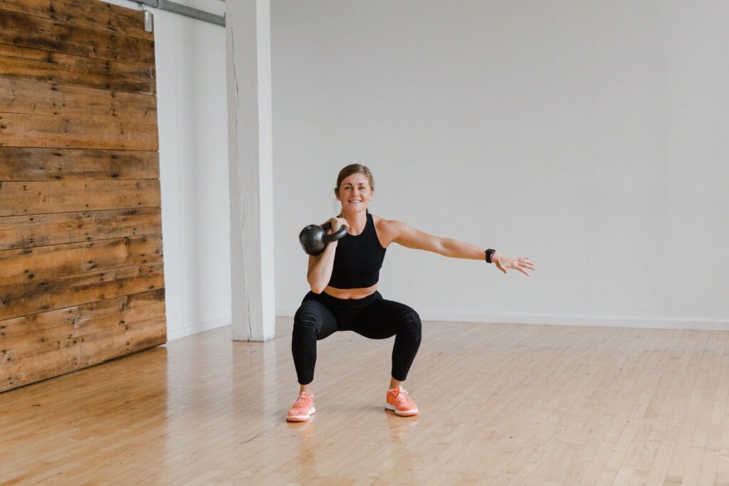 Woman performing a Front Rack Squat + Single Arm Thruster | kettlebell leg workout