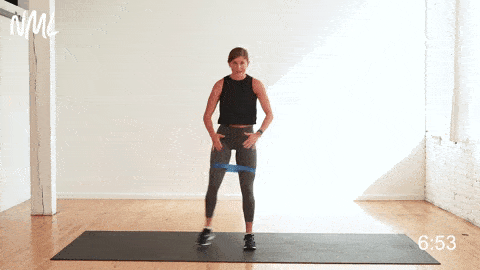 woman performing side to side squats with a resistance band in a leg workout at home