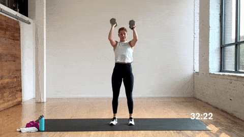 woman performing a clean and overhead press using dumbbells in a free weight workout