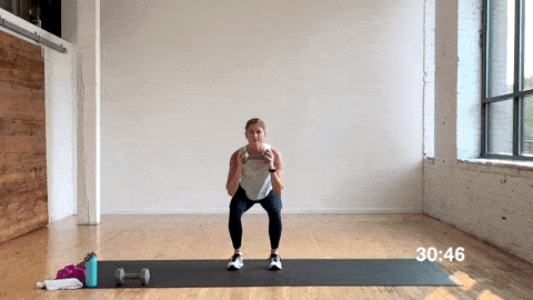 woman performing a 2 pulse squat and 2 press jacks with dumbbells in a free weight workout