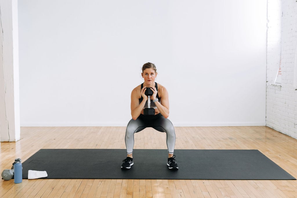 Women performing a squat hold with a dumbbell at heart center during a leg and back workout. 