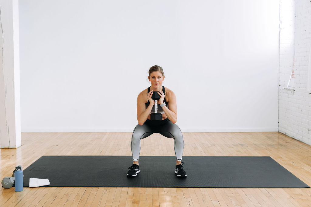 Women performing a squat hold with a dumbbell at heart center during a leg and back workout. 