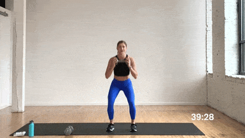 woman performing a squat hold and dumbbell press out in a full body workout at home