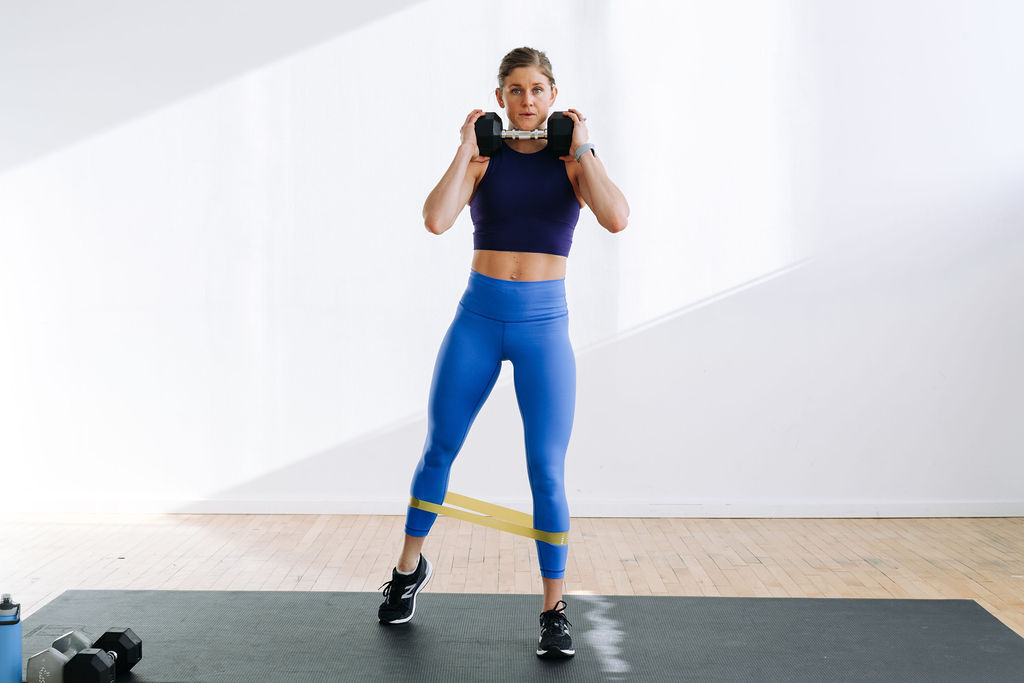 Women doing a split squat, holding a dumbbell at heart center during a leg workout at home. Best leg workouts. 