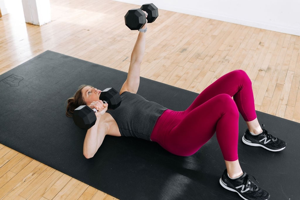 Woman performing a dumbbell chest press as part of a 30-minute upper body push workout at home