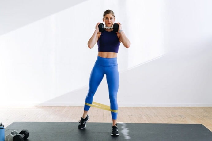 woman performing a squat with a dumbbell and resistance band in a leg workout
