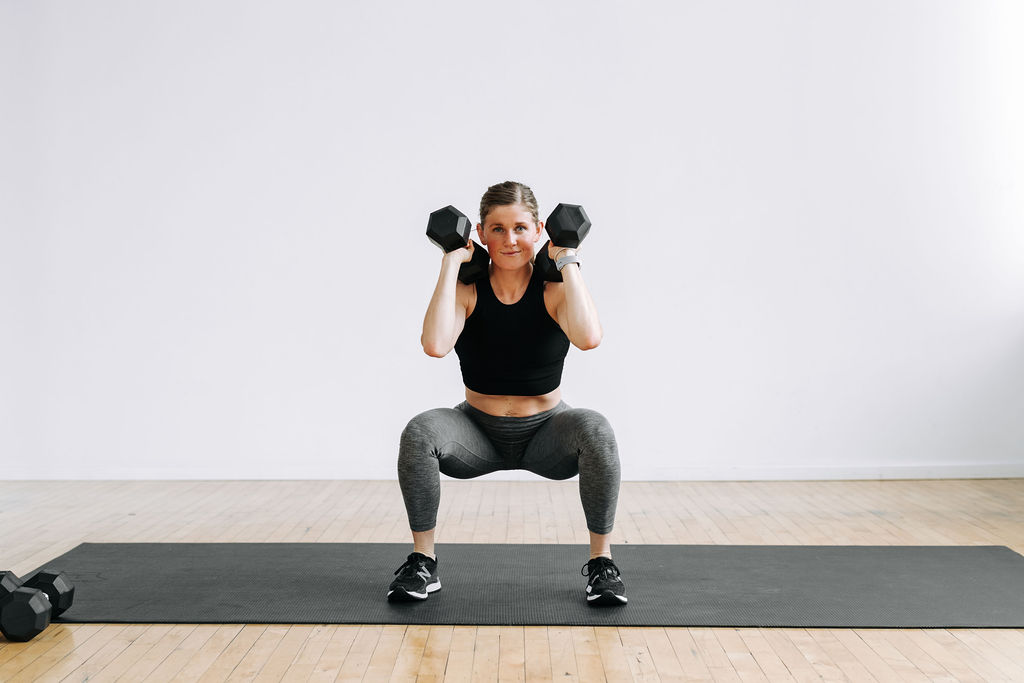 woman performing a low squat hold with dumbbell front racked in a HIIT workout