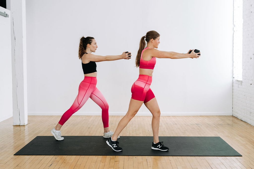 two women performing a wood chop with dumbbells in a cardio abs workout