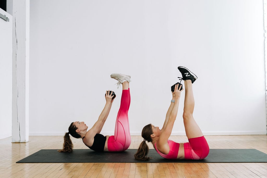 HIIT Core Workout | two women performing a crunch with dumbbell