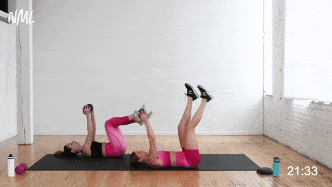 two women performing a lying pull over and touch touch as part of an abs workout