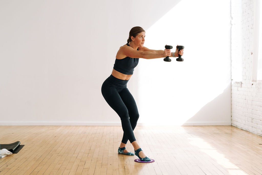 woman performing a dumbbell chest press and leg sweep with exercise slider in a barre workout