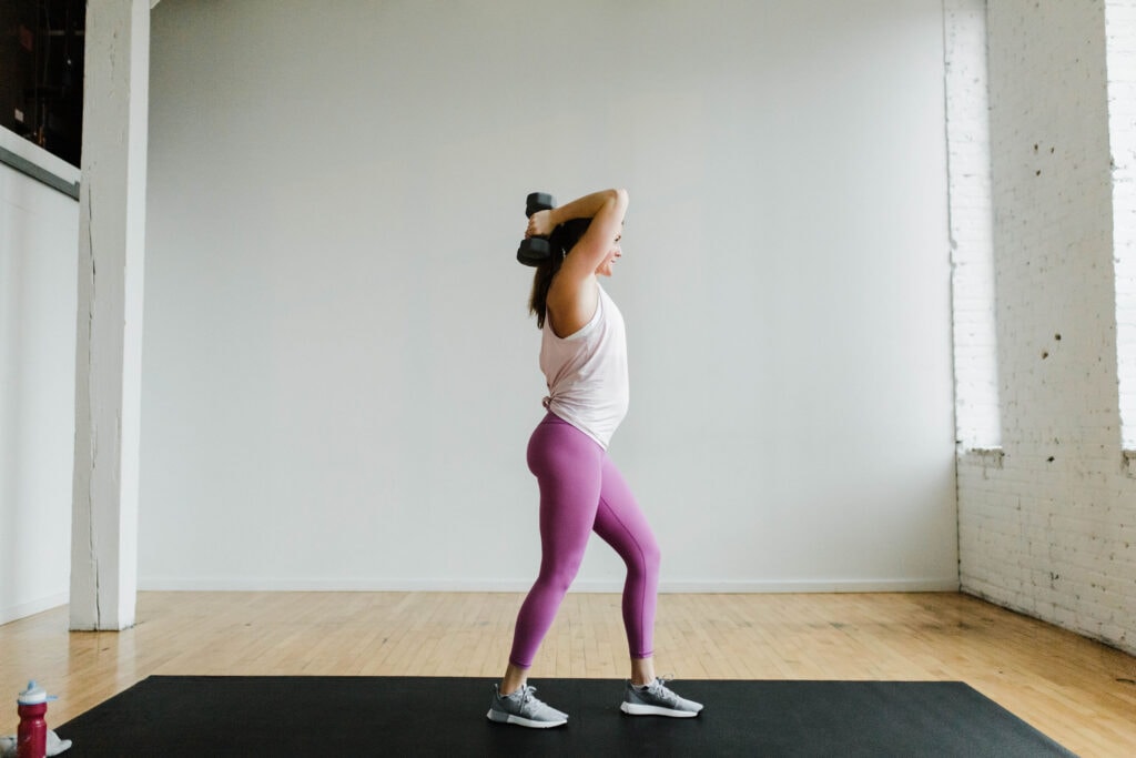 Woman performing overhead tricep extensions with dumbbells in a 30 Minute Arm Workout with Weights