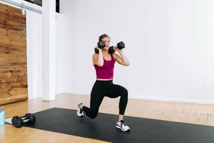 A women doing a split lunge with two dumbbells racked at her shoulders.