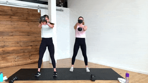 one woman performing kettlebell swings with a kettlebell and one woman performing swings with a single dumbbell in a cardio workout at home