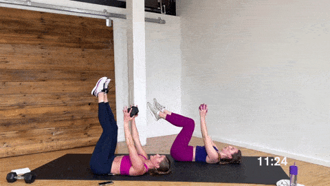 two women performing an overhead lat extension and dumbbell pullover with leg raise in a home workout for women