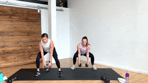 two women performing a kettlebell clean and squat jack in a kettlebell cardio workout at home