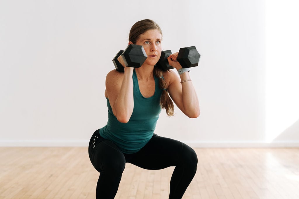 Woman performing a dumbbell squat with two dumbbells racked at her shoulders as part of the best dumbbell HIIT exercises