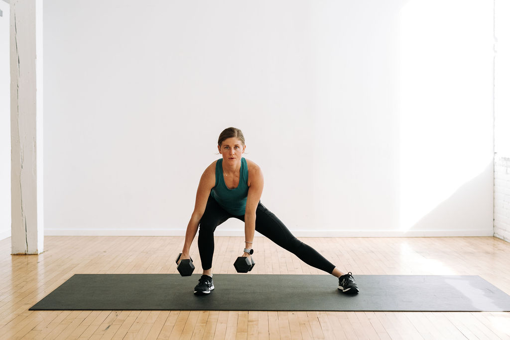 Woman performing a lateral lunge with dumbbells in a full body dumbbell HIIT workout