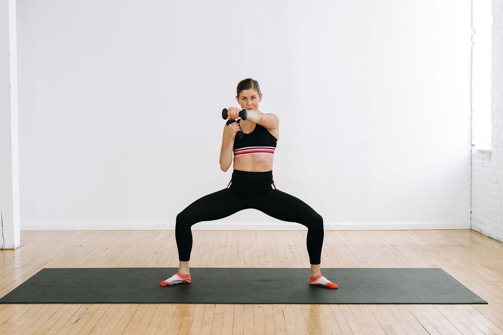 woman performing a low sumo squat hold and punch as part of the best barre workouts at home