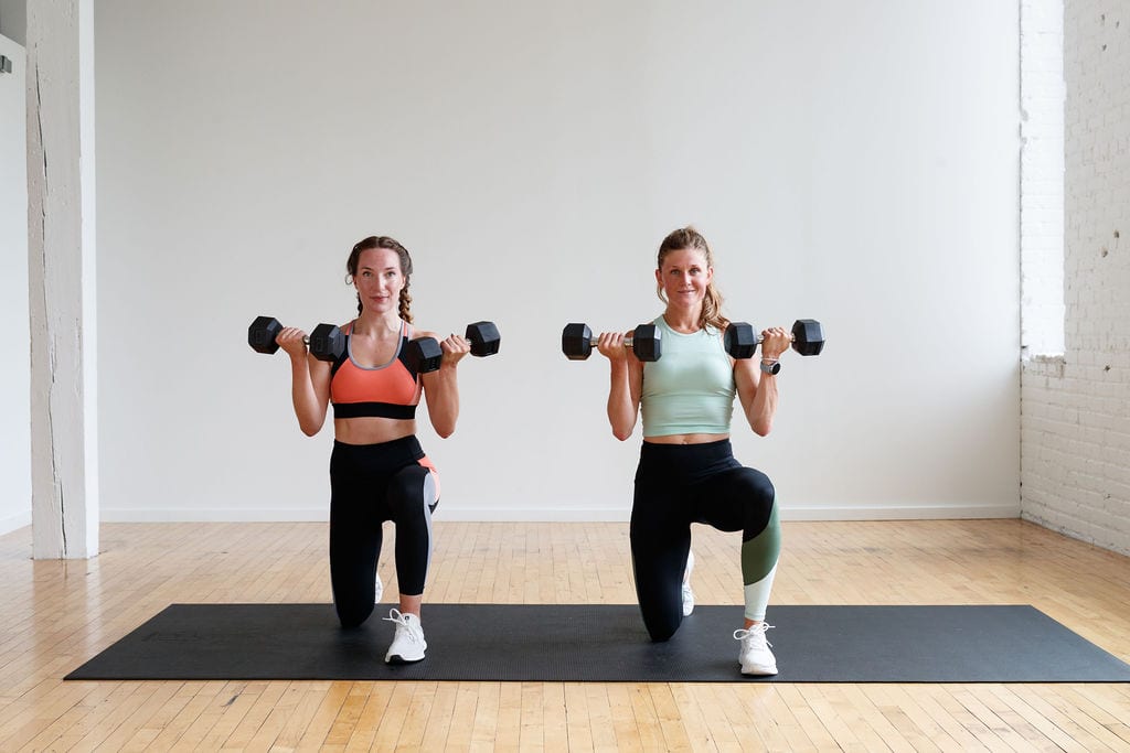 two women performing a half kneeling bicep curl with dumbbells in a HIIT workout at home for women