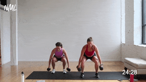 two women performing a dumbbell squat and squat hold in a HIIT workout at home