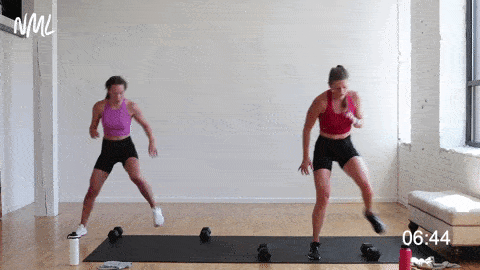 two women performing a lateral shuffle over dumbbells in a high intensity workout at home