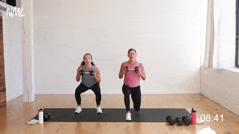 two women, one pregnant, performing a lunge hold and dumbbell press as part of a pregnancy workout for the first trimester