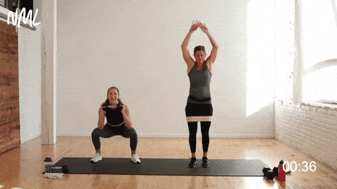 two women performing squat jacks in a leg workout at home