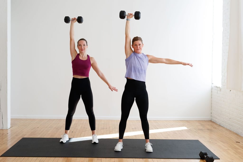 two women performing a single arm overhead dumbbell press in a first trimester HIIT workout