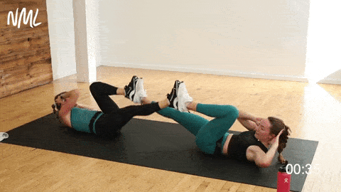 two women performing bicycle crunches with a partner in a bodyweight workout