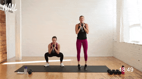 two women performing goblet squat jacks in a leg superset workout