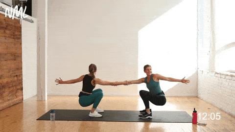 two women performing a partner squat and rotation as part of partner exercises at home