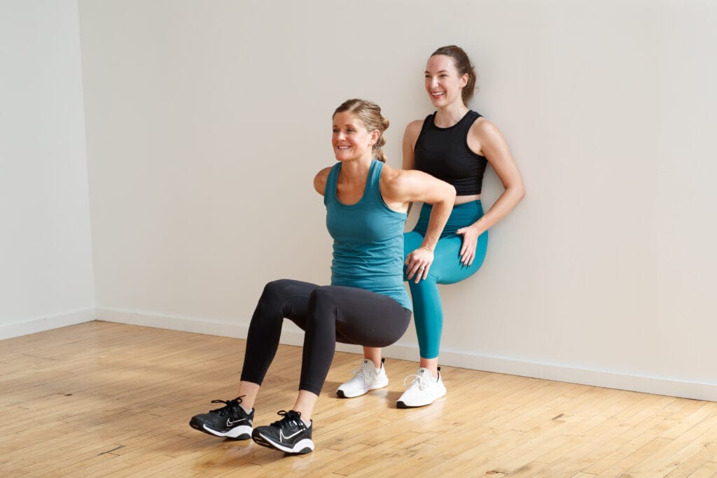 women performing tricep dips and wall sit with a partner in a partner workout at home