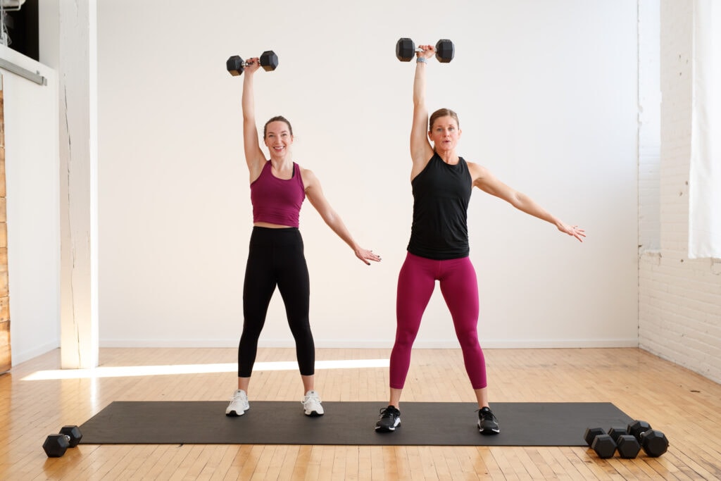 two women performing a single arm overhead press in a superset workout
