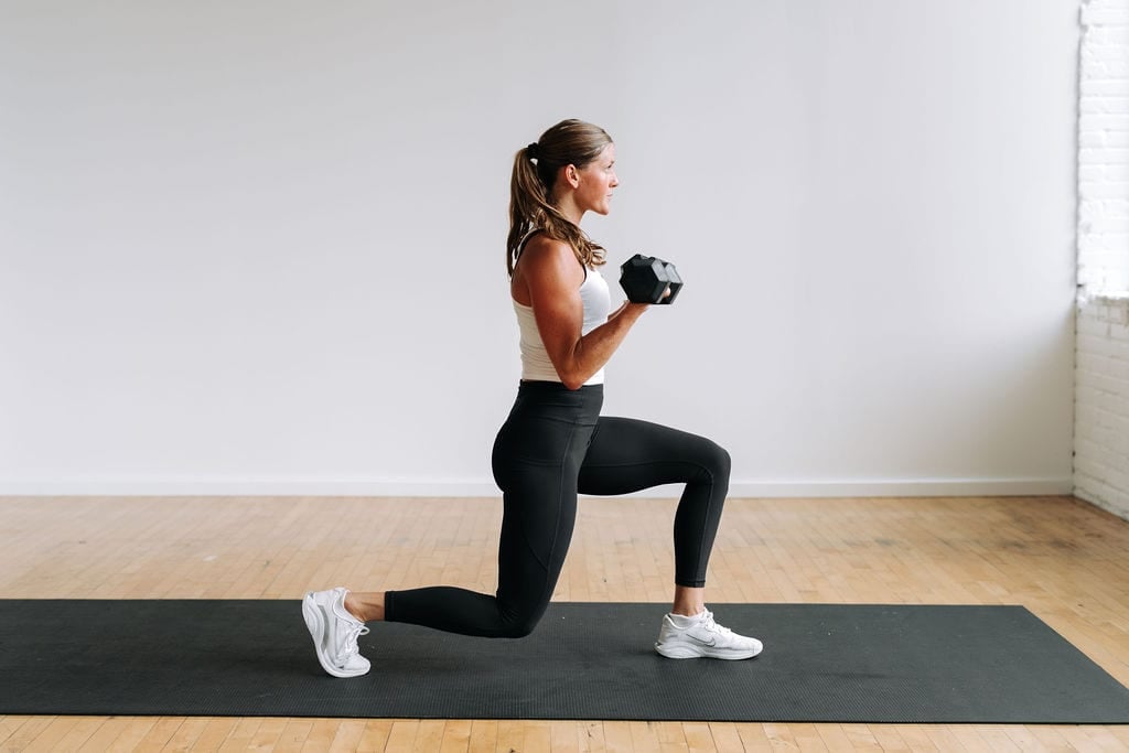 woman performing a lunge and bicep curl with dumbbells as part of a full body HIIT workout